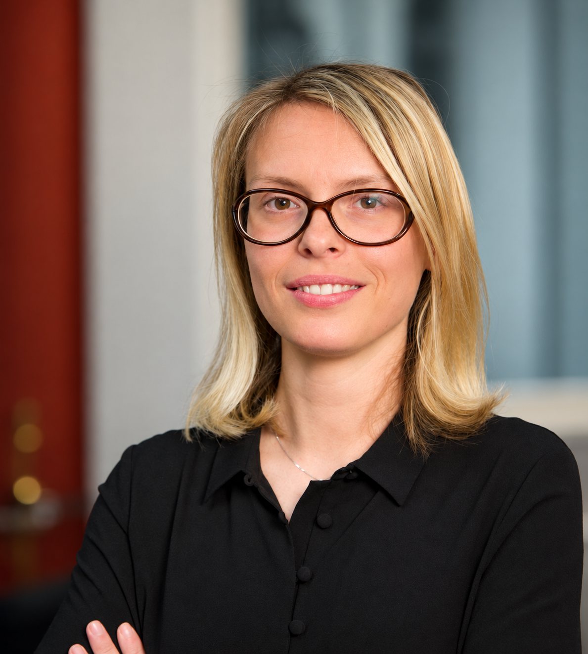 Portrait de Mélanie Tastevin, souriante, cheveux blonds, lunettes et chemise noire.